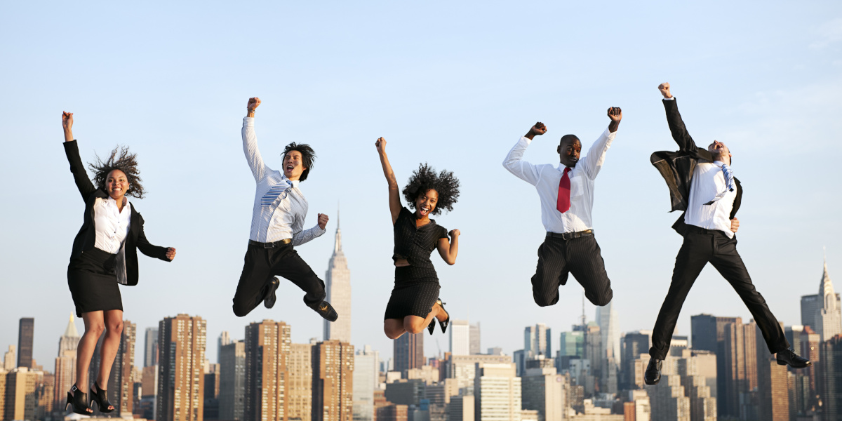 People in business attire jumping in the air with their fists raised in excitement with the New York Skyline in the background