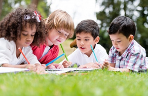 Children laying on grass, writing on paper