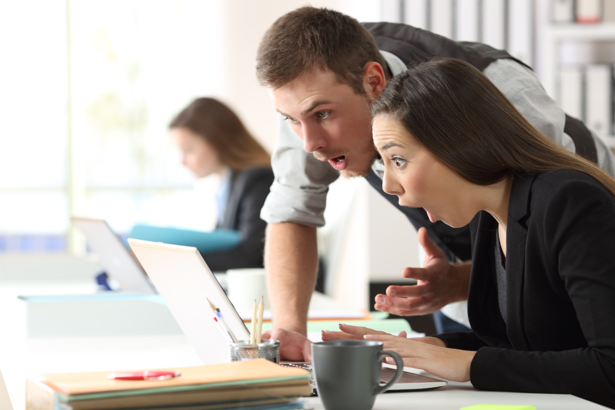 Two Surprised Coworkers Reading News on Laptop Computer at Office