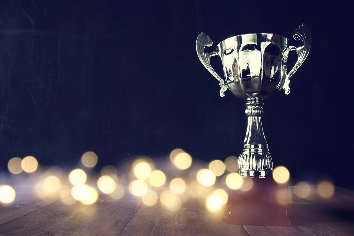 A silver trophy standing on wooden table with light around the base, as it reflects people working at the office on it's surface