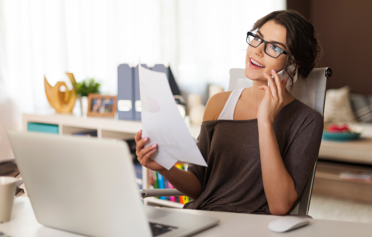 Woman on Phone Seated in Front of Computer in Home Office