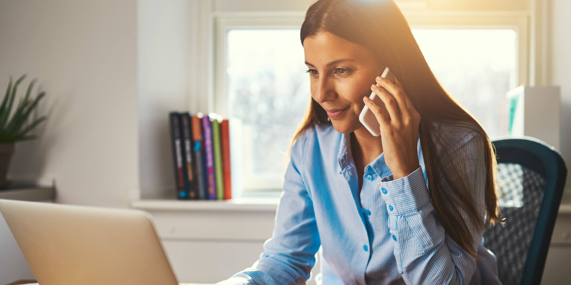 Woman using mobile phone while working in front of a laptop