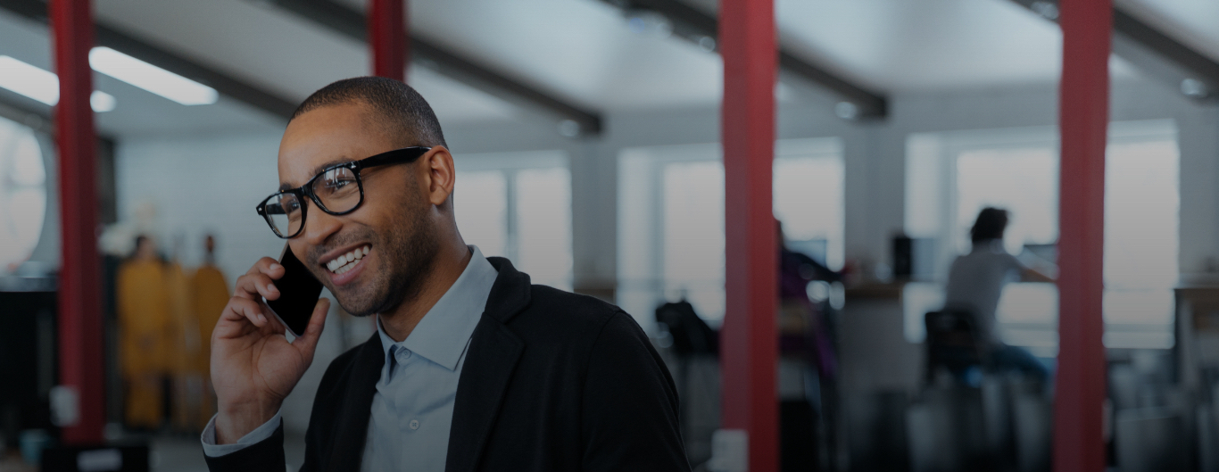 Man wearing glasses and holding mobile phone, against a blurred interior background