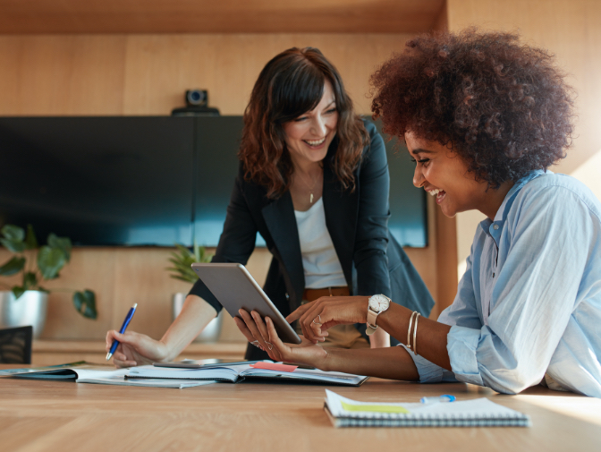 Two smiling businesswomen looking at a tablet device together